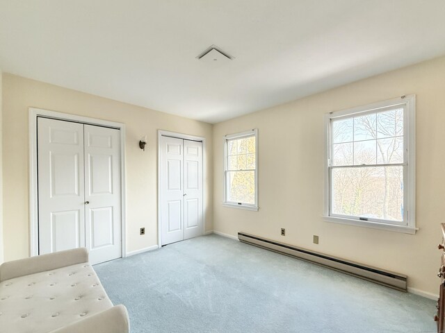 unfurnished bedroom featuring baseboard heating, light colored carpet, and multiple closets