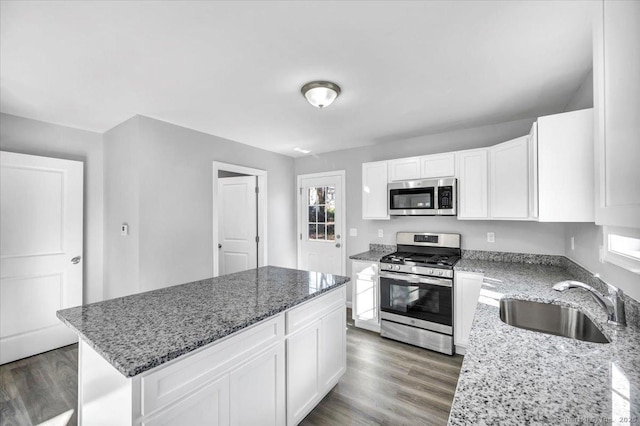 kitchen with appliances with stainless steel finishes, sink, white cabinets, a center island, and light stone counters