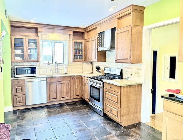 kitchen with wall chimney exhaust hood, sink, light stone counters, appliances with stainless steel finishes, and backsplash