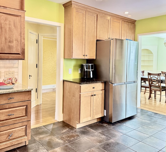 kitchen with stainless steel refrigerator, tasteful backsplash, and dark stone countertops