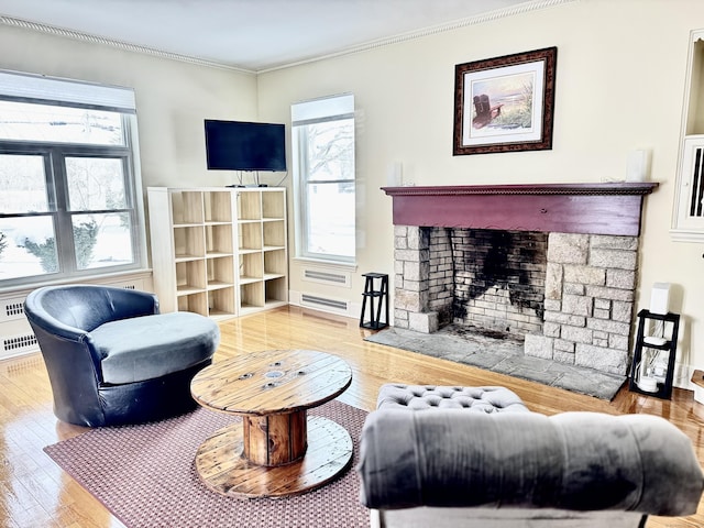 living room with hardwood / wood-style flooring, ornamental molding, and a stone fireplace