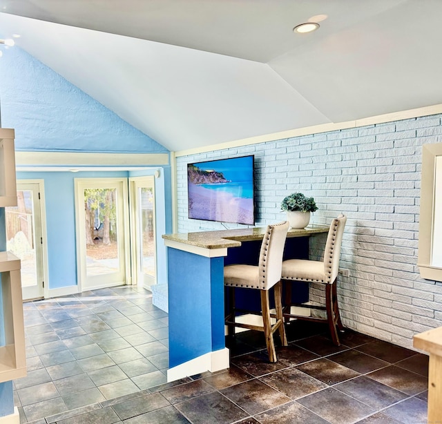 home office featuring lofted ceiling and brick wall