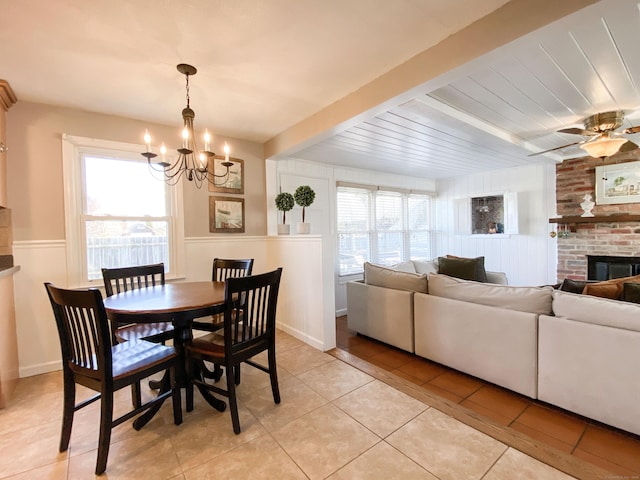 dining space with light tile patterned flooring, a fireplace, beam ceiling, and ceiling fan with notable chandelier