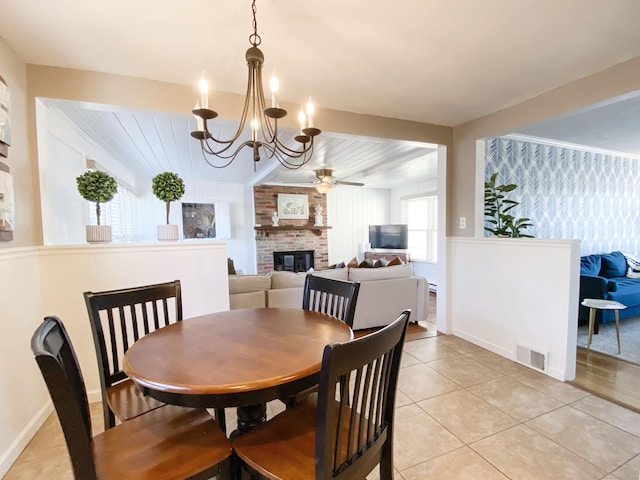 tiled dining space with ceiling fan with notable chandelier and a brick fireplace