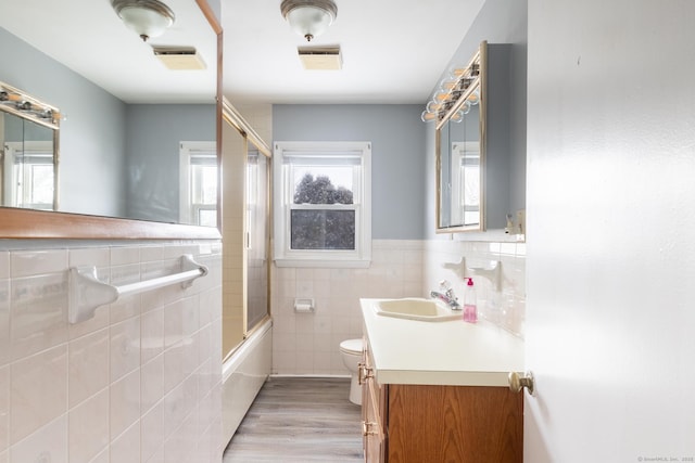 full bathroom with combined bath / shower with glass door, tile walls, hardwood / wood-style flooring, vanity, and toilet