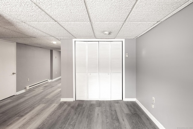 unfurnished bedroom featuring hardwood / wood-style flooring, a baseboard radiator, a closet, and a paneled ceiling