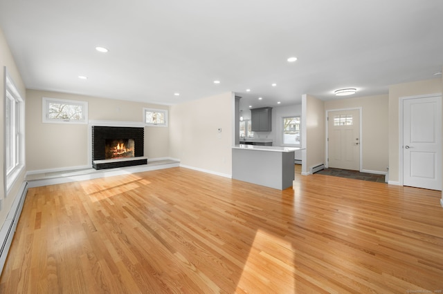 unfurnished living room featuring a baseboard radiator, a fireplace, and light hardwood / wood-style floors