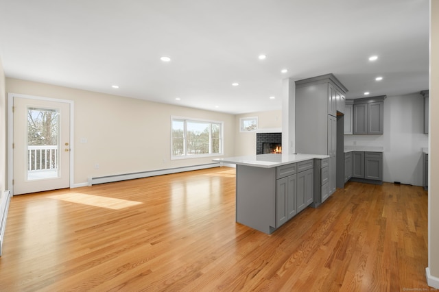 kitchen with gray cabinets, a brick fireplace, a baseboard radiator, kitchen peninsula, and light wood-type flooring