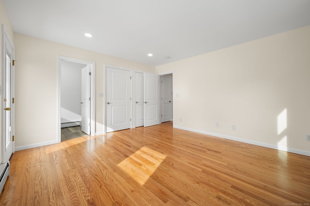 unfurnished bedroom with ensuite bathroom, a baseboard heating unit, and light wood-type flooring