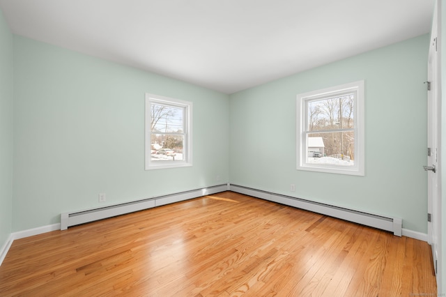 empty room featuring a baseboard heating unit, a wealth of natural light, and light hardwood / wood-style flooring