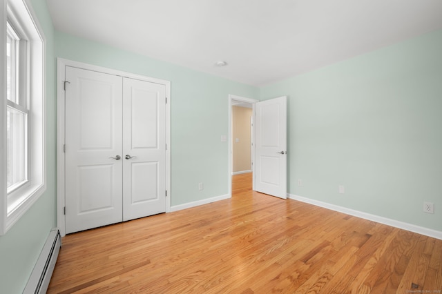 unfurnished bedroom featuring a baseboard heating unit, a closet, and light wood-type flooring