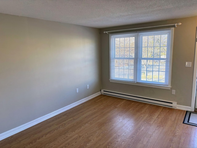 spare room featuring a textured ceiling, baseboard heating, and light hardwood / wood-style floors