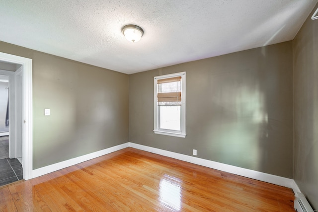 empty room featuring hardwood / wood-style floors, a textured ceiling, and a baseboard heating unit