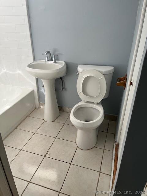 bathroom with a tub to relax in, toilet, and tile patterned flooring