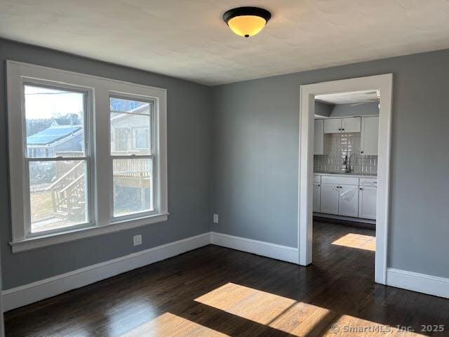 unfurnished room with sink, dark wood-type flooring, and a wealth of natural light