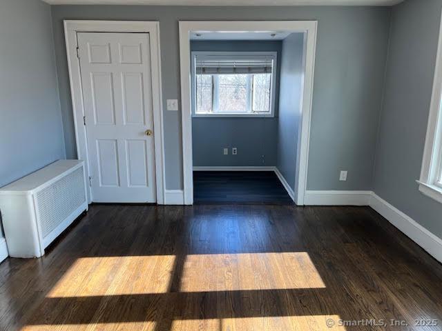 unfurnished room featuring radiator heating unit and dark hardwood / wood-style floors