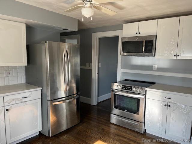 kitchen with dark wood-type flooring, stainless steel appliances, tasteful backsplash, and white cabinets