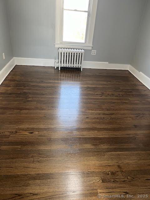 empty room with dark hardwood / wood-style flooring and radiator