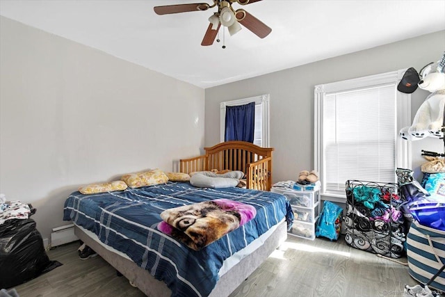 bedroom featuring a baseboard heating unit, wood-type flooring, and ceiling fan