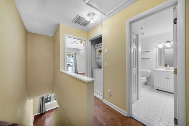 hallway with stacked washer and dryer, attic access, visible vents, an upstairs landing, and a sink