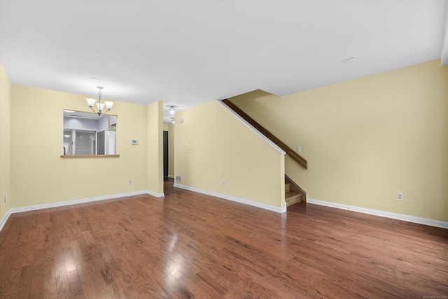 unfurnished living room with wood finished floors, a notable chandelier, baseboards, and stairs