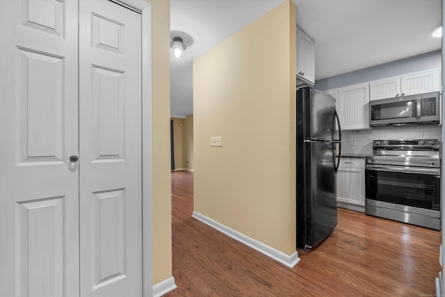 kitchen with wood finished floors, appliances with stainless steel finishes, backsplash, and white cabinetry