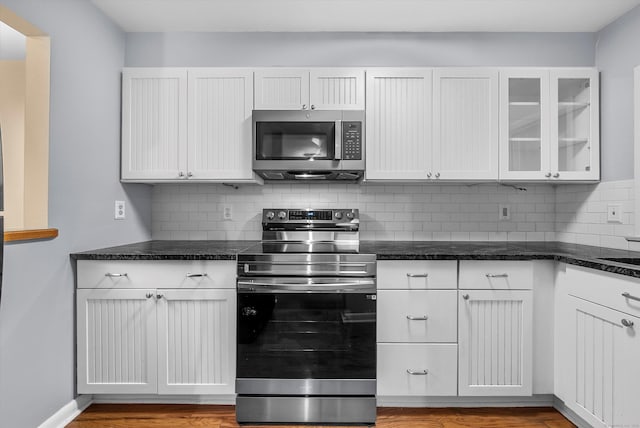 kitchen with stainless steel appliances, dark stone counters, white cabinets, and tasteful backsplash