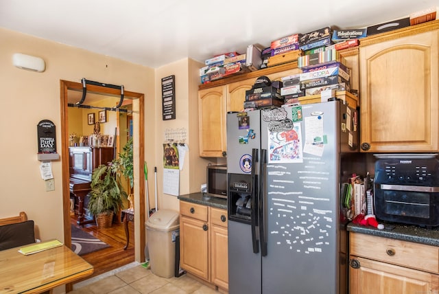 kitchen with stainless steel appliances, light tile patterned flooring, dark stone countertops, and light brown cabinetry