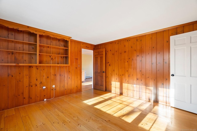 unfurnished room featuring wood-type flooring, wooden walls, and a baseboard radiator