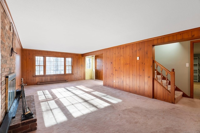 unfurnished living room featuring crown molding, light carpet, wooden walls, a fireplace, and a baseboard heating unit