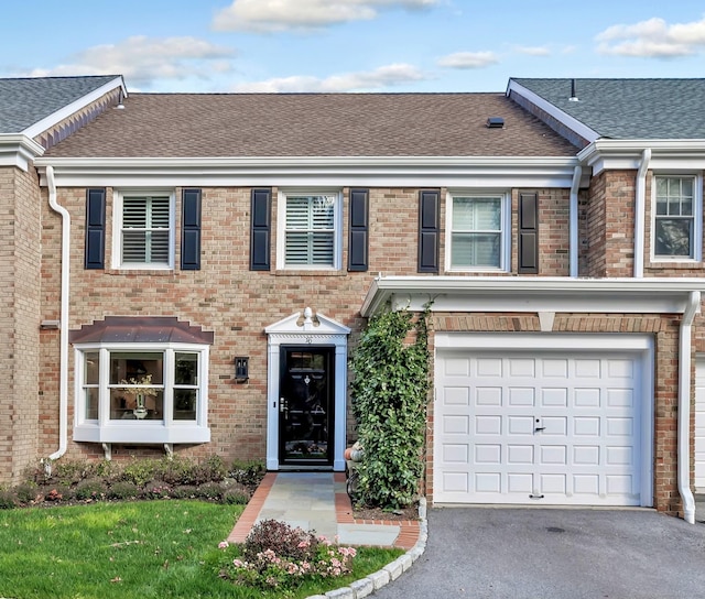 view of property with driveway, a shingled roof, an attached garage, and brick siding