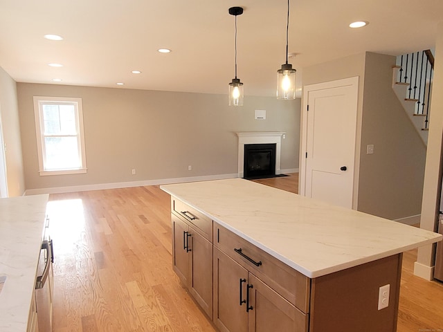 kitchen featuring decorative light fixtures, light stone countertops, a kitchen island, and light wood-type flooring