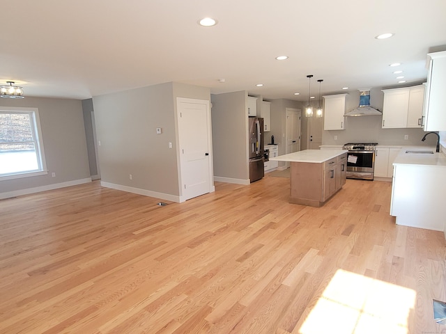 kitchen featuring white cabinetry, hanging light fixtures, a center island, stainless steel appliances, and wall chimney range hood