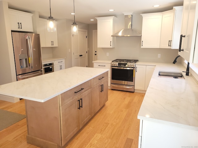 kitchen featuring white cabinets, appliances with stainless steel finishes, a kitchen island, and wall chimney range hood