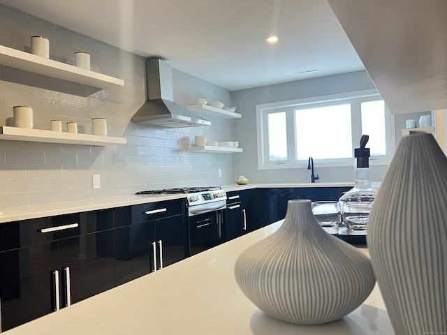 kitchen featuring gas range, wall chimney range hood, decorative backsplash, and sink