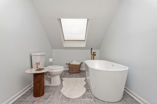 bathroom with vaulted ceiling with skylight, tile patterned floors, a tub, and toilet