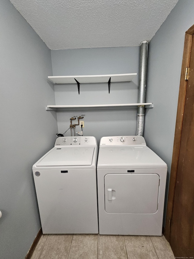 laundry area featuring light tile patterned flooring, a textured ceiling, and washer and clothes dryer