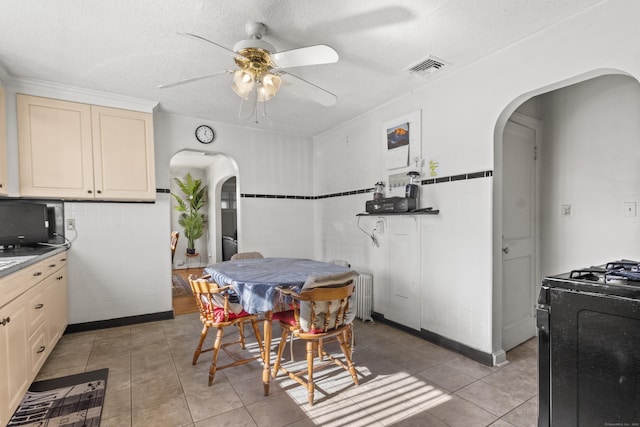 kitchen featuring gas stove, a textured ceiling, light tile patterned floors, radiator, and cream cabinetry