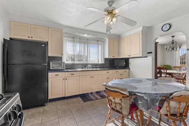 kitchen featuring stainless steel range oven, sink, black fridge, light tile patterned floors, and cream cabinetry