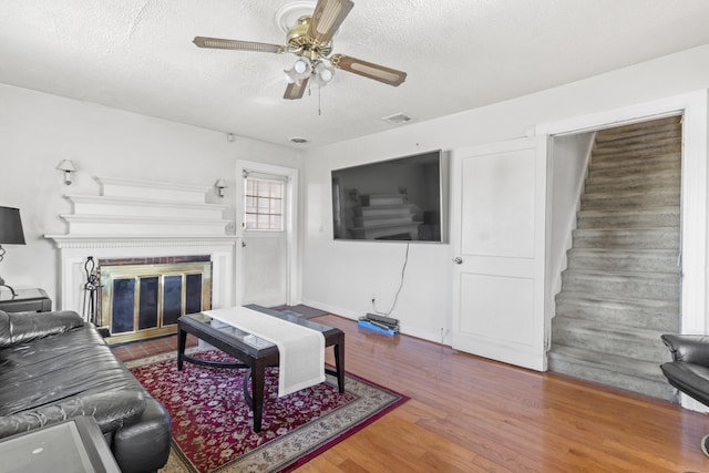 living room with hardwood / wood-style flooring, ceiling fan, and a textured ceiling