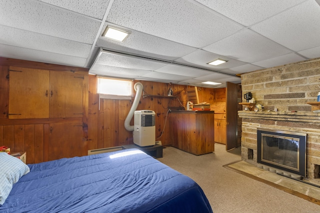 carpeted bedroom featuring baseboard heating, a large fireplace, a drop ceiling, and wood walls