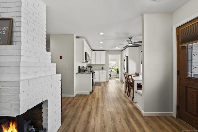 interior space featuring ceiling fan, wood-type flooring, and a brick fireplace