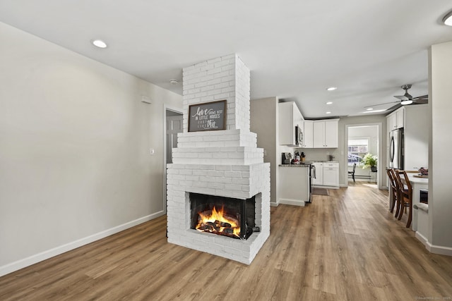 living room with wood-type flooring, ceiling fan, and a fireplace