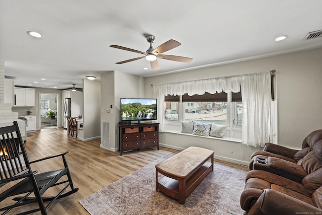 living room with ceiling fan, a large fireplace, and light hardwood / wood-style floors