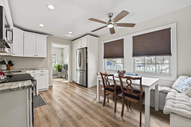 kitchen featuring white cabinetry, light wood-type flooring, appliances with stainless steel finishes, ceiling fan, and light stone countertops