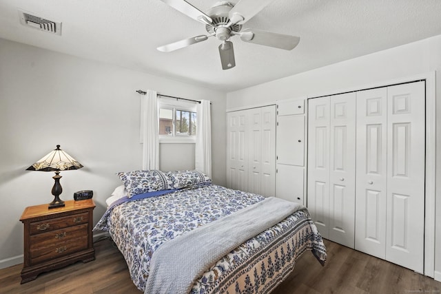 bedroom with ceiling fan, a textured ceiling, dark hardwood / wood-style floors, and multiple closets