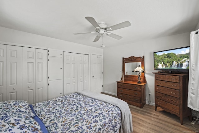 bedroom featuring two closets, wood-type flooring, and ceiling fan