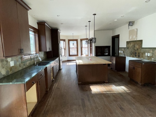 kitchen featuring sink, stainless steel refrigerator, dark hardwood / wood-style floors, a center island, and decorative light fixtures