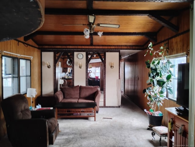 living room featuring beamed ceiling, wood walls, a ceiling fan, and carpet floors