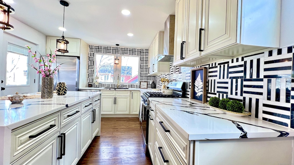 kitchen with hanging light fixtures, stainless steel appliances, a center island, light stone counters, and wall chimney exhaust hood